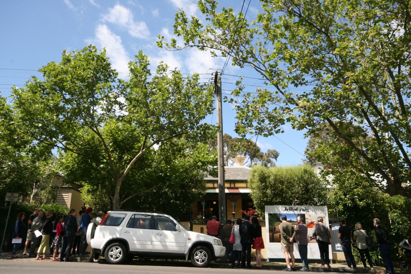 Prospective buyers gathered on a leafy Melbourne street for a residential auction outside a Victorian-era weatherboard home.